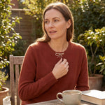 A woman in an orange sweater wearing a handmade silver wavy pendant with a green tourmaline gemstone while sitting in a sunlit garden.