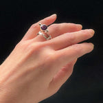 Hand wearing a silver ring with a purple gemstone on a black background