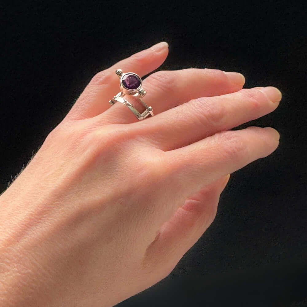 Hand wearing a silver ring with a purple gemstone on a black background