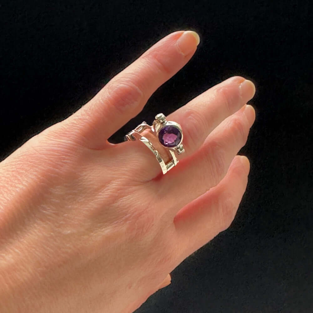 Silver ring with a purple gemstone on a hand against a black background