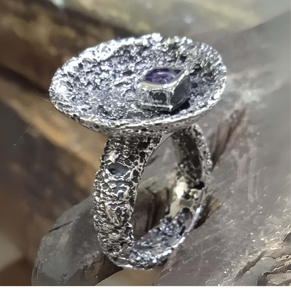 Silver ring with an amethyst on a stone surface