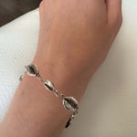 Silver bracelet with shell-like charms on a wrist against a neutral background