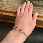 Hand wearing a silver bracelet with carved amethyst against a wooden background