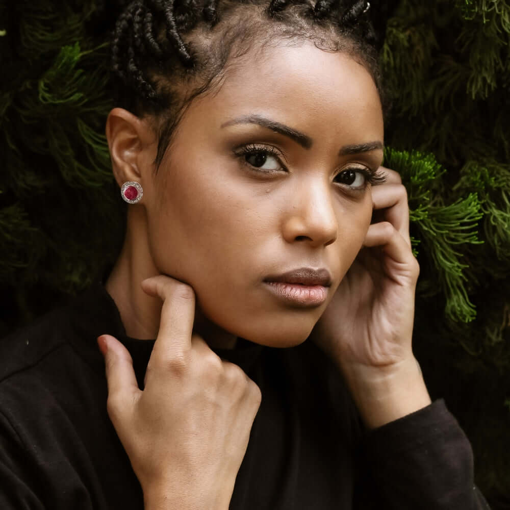 Woman with red coral earrings posing against a green foliage background