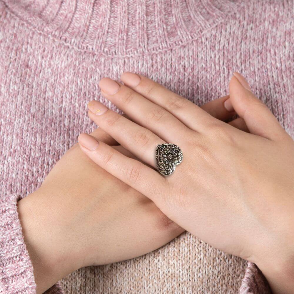 Hand wearing a decorative silver ring on a pink textured fabric background