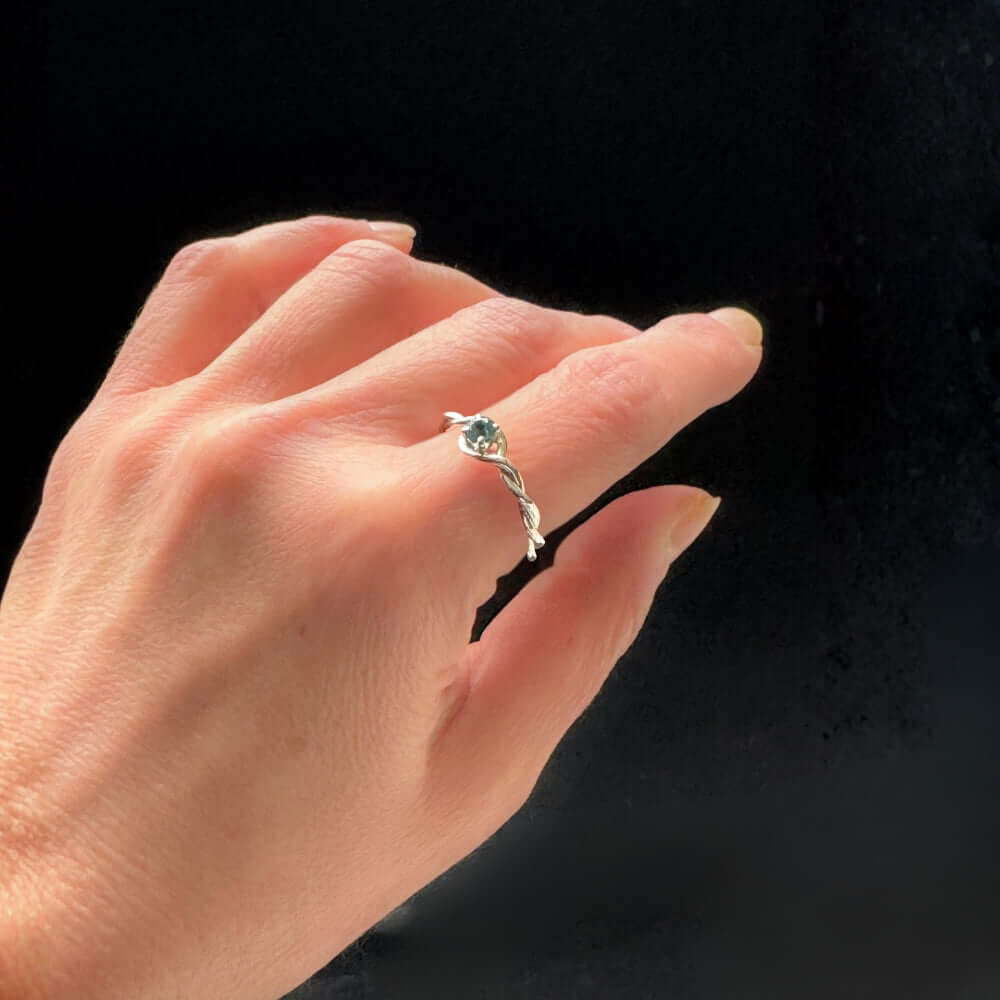 Hand wearing a silver ring with a blue gemstone on a black background
