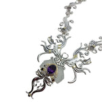 Ornate silver necklace with a purple gemstone on a white background side view