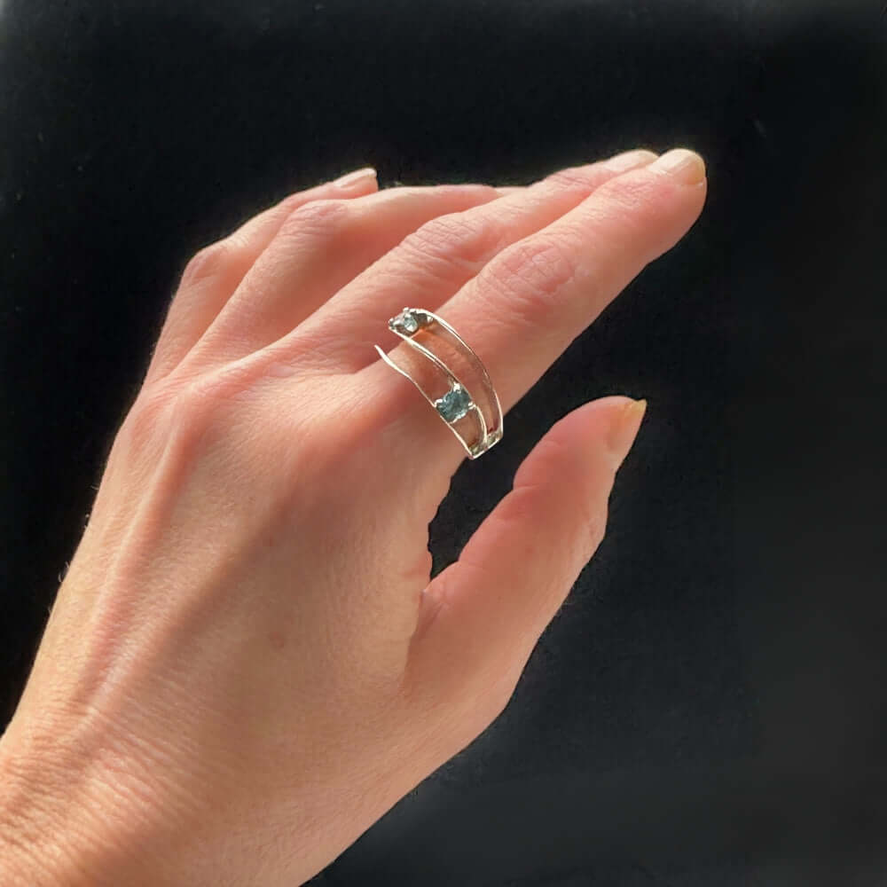 Hand wearing a silver ring with two blue gemstones on a black background