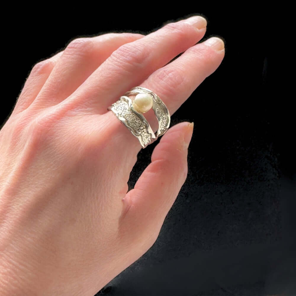 Hand wearing a Taxco silver ring with a pearl on a black background