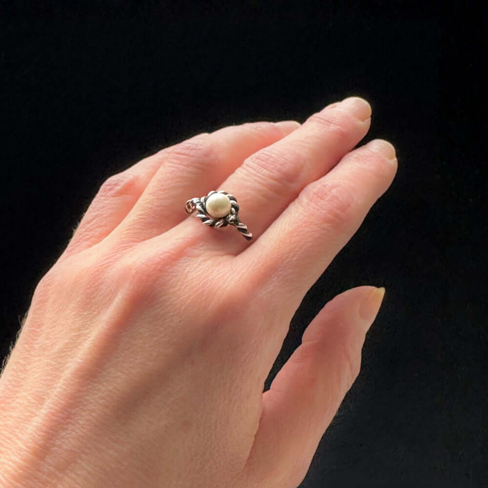Hand wearing a silver ring with a pearl on a black background