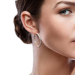 Close-up of a woman wearing silver hoop earrings with a neutral background