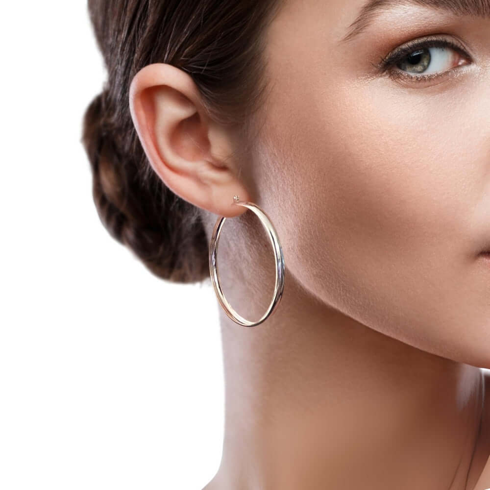 Close-up of a woman wearing silver hoop earrings with a neutral background