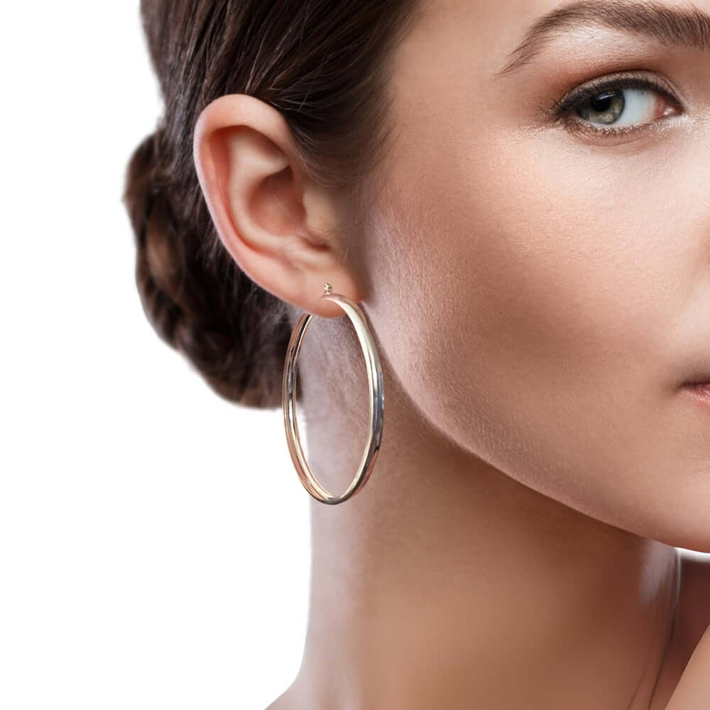 Close-up of a woman wearing silver hoop earrings with a neutral background