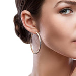 Close-up of a woman wearing silver hoop earrings with a neutral background