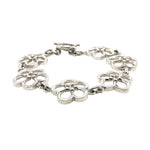 A silver bracelet featuring a series of openwork floral-like links connected by small chain segments, with a toggle clasp, shown on a plain white background.