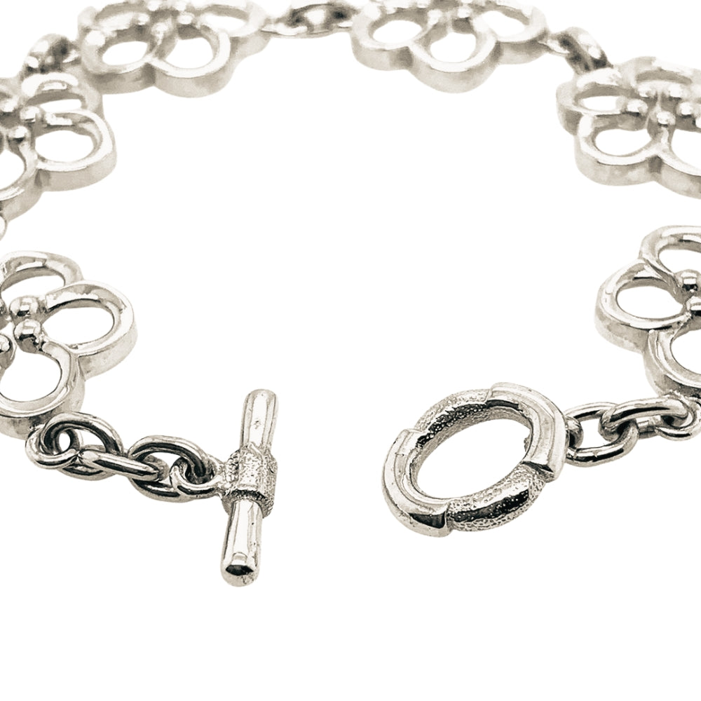 A silver-tone chain bracelet with repeating openwork floral links and a toggle clasp, photographed on a plain white background.