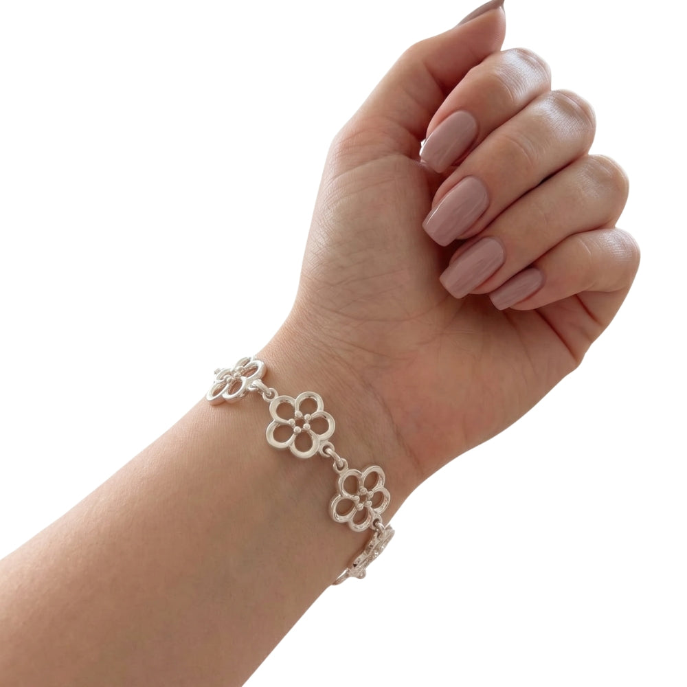 A silver bracelet with openwork floral links worn on a person's wrist, shown against a plain white background.