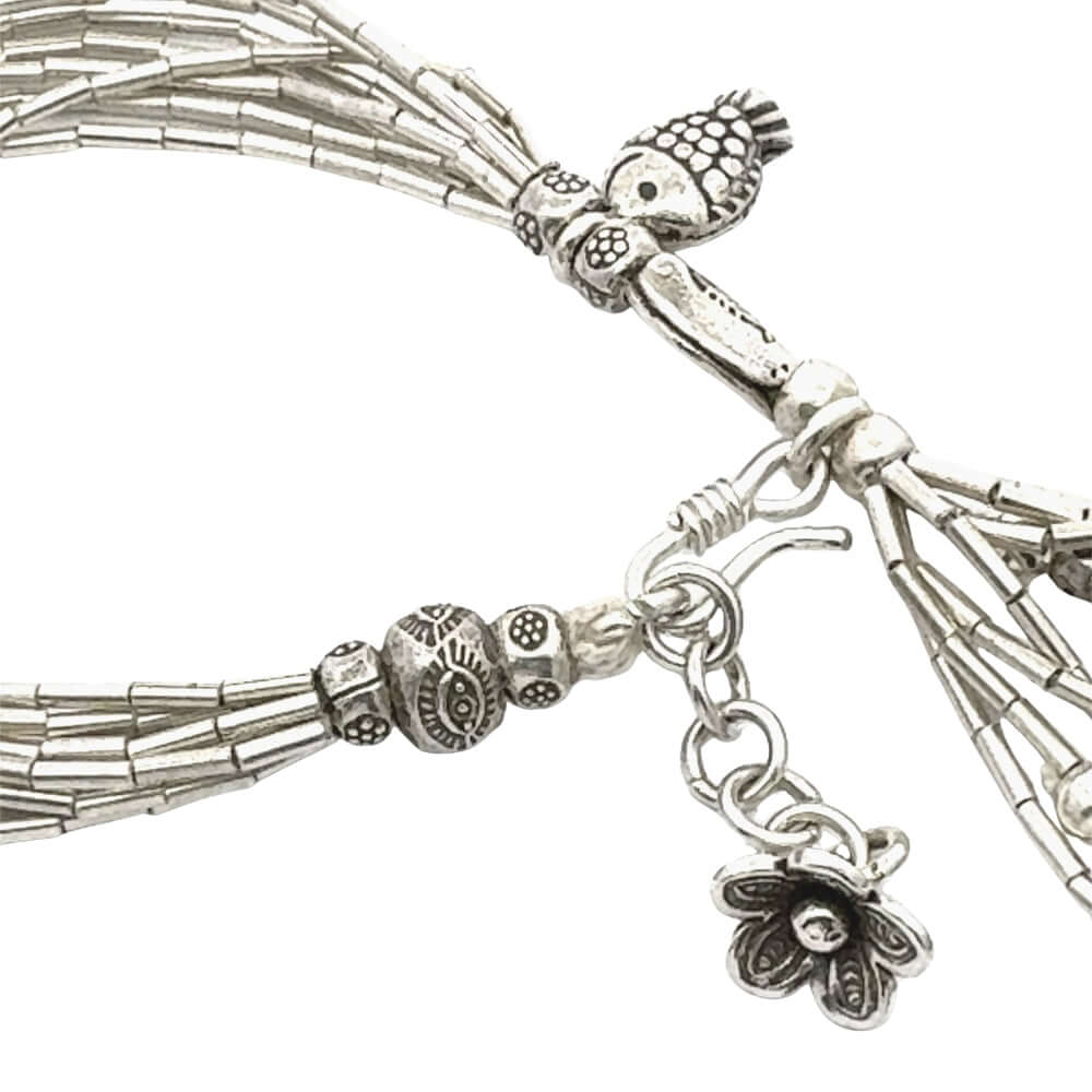 Silver beaded bracelet with tassels and floral charm on a white background