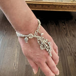 Hand wearing a silver bracelet with charms on a wooden surface