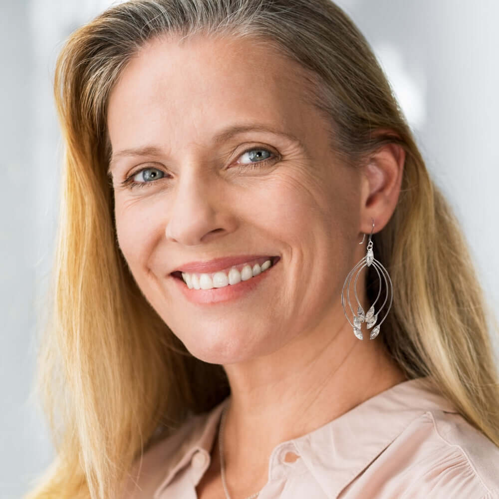 Woman with blonde hair and silver earrings smiling against a light background