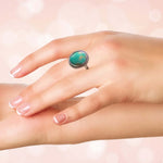 Turquoise silver ring on a hand against a soft pink background