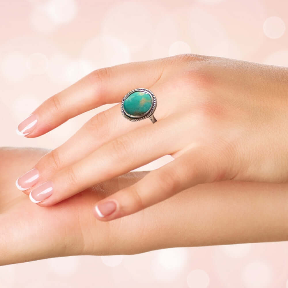 Turquoise silver ring on a hand against a soft pink background