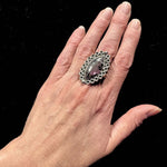 Hand wearing a decorative silver ring on a black background