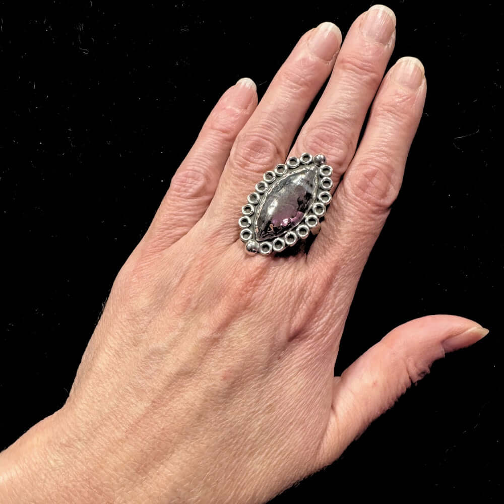Hand wearing a decorative silver ring on a black background