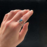 Hand wearing a silver ring with a blue stone on a black background