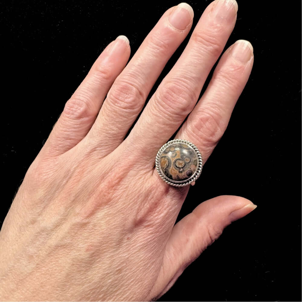 Hand wearing a silver ring with a large round stone on a black background