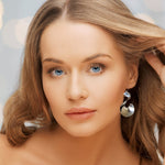 Woman with blue eyes and blonde hair wearing silver earrings against a neutral background