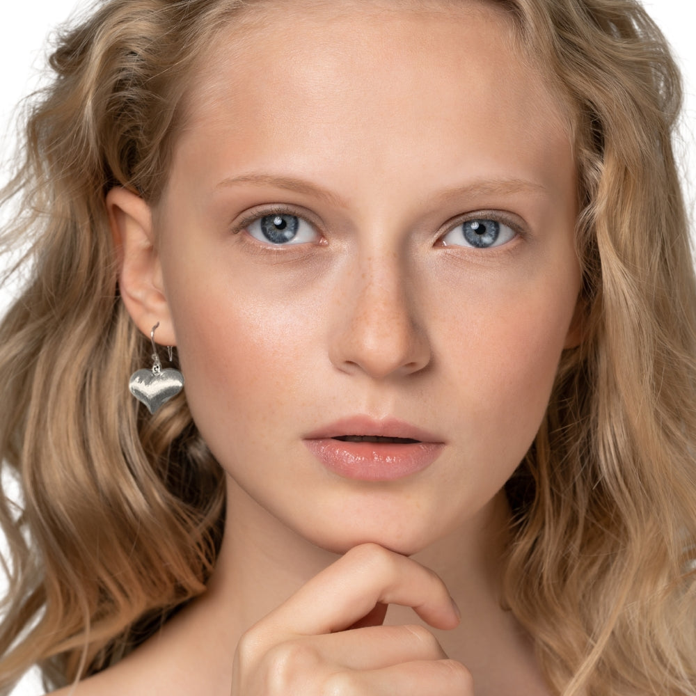 Close-up of a woman wearing a silver heart earring on a white background