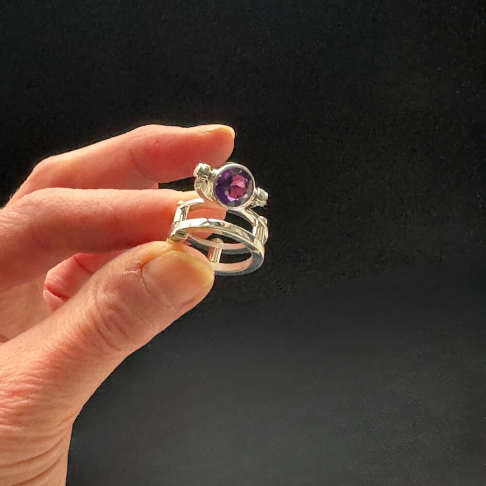 950 Silver ring with a purple gemstone held by a hand against a black background