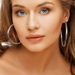 Close-up of a woman wearing large hoop silver earrings with a neutral background