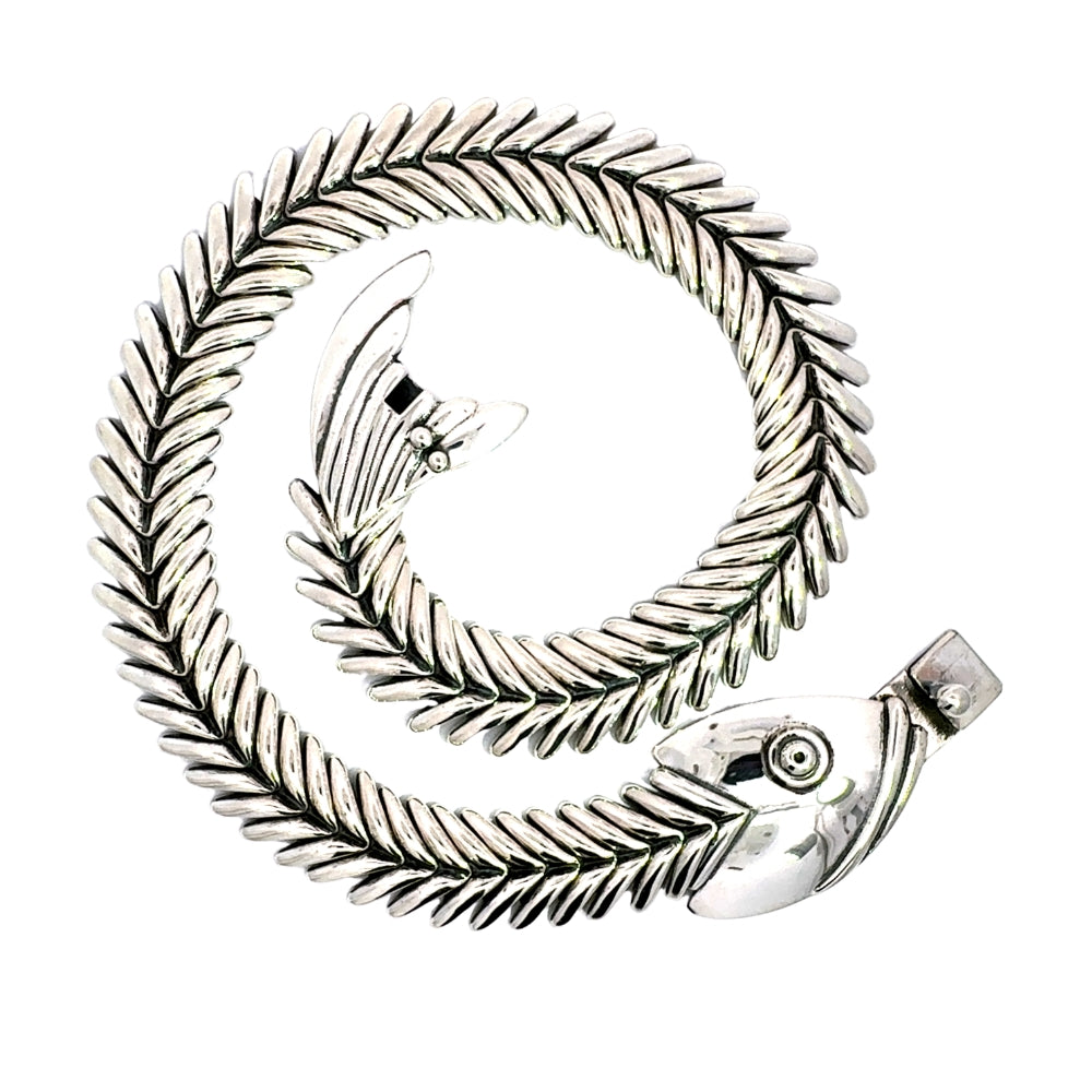 The articulated sterling silver fishbone necklace coiled into a spiral, showcasing the design details of the fish head and tail on a clean white background.