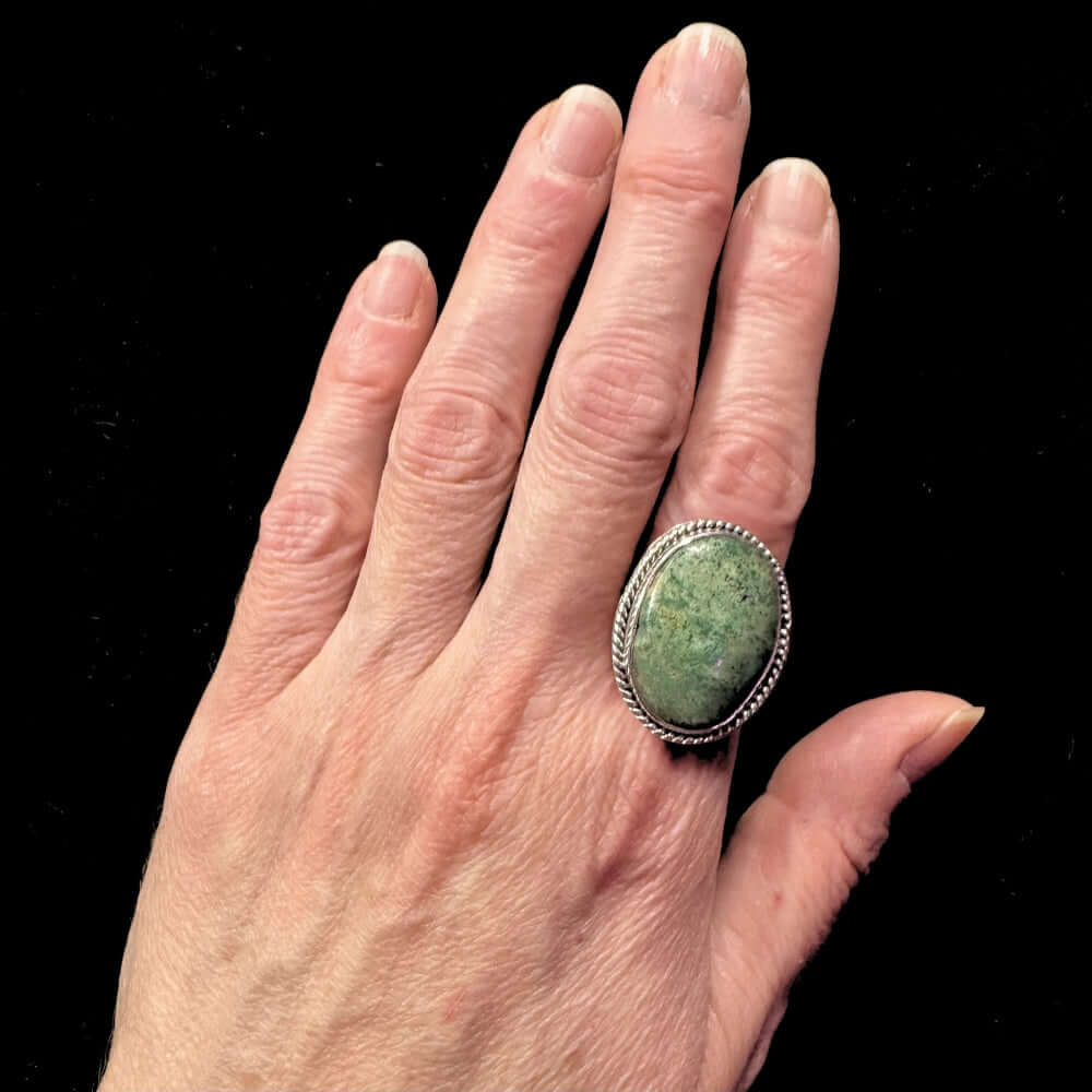 Hand wearing a green stone ring with a black background