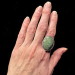 Hand wearing a green stone ring with a black background