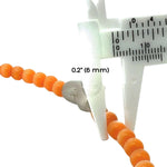 Orange cats eye beads being measured with a caliper on a white background