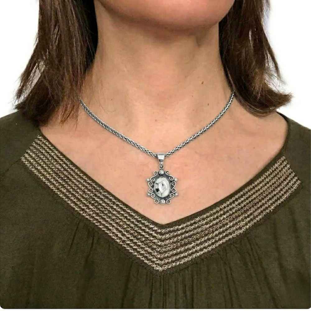 Person wearing a silver necklace with a pendant on a plain background