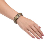 A close-up of a person's hand and wrist wearing a wide silver cuff bracelet with a gold crackle pattern, set against a plain white background.