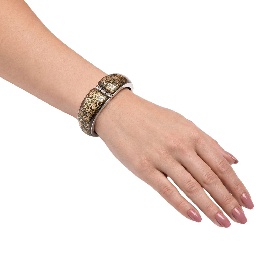 A close-up of a person's hand and wrist wearing a wide silver cuff bracelet with a gold crackle pattern, set against a plain white background.