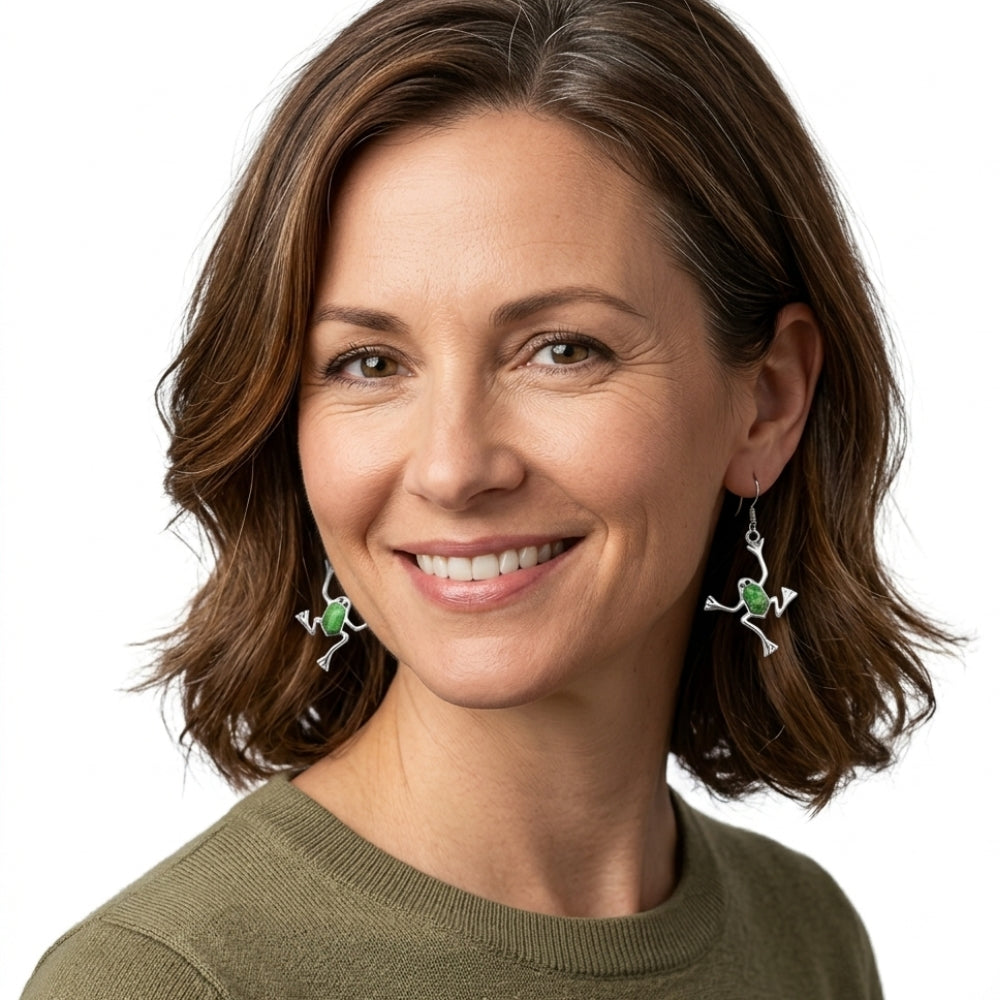 Woman wearing silver frog earrings with green turquoise with a plain background
