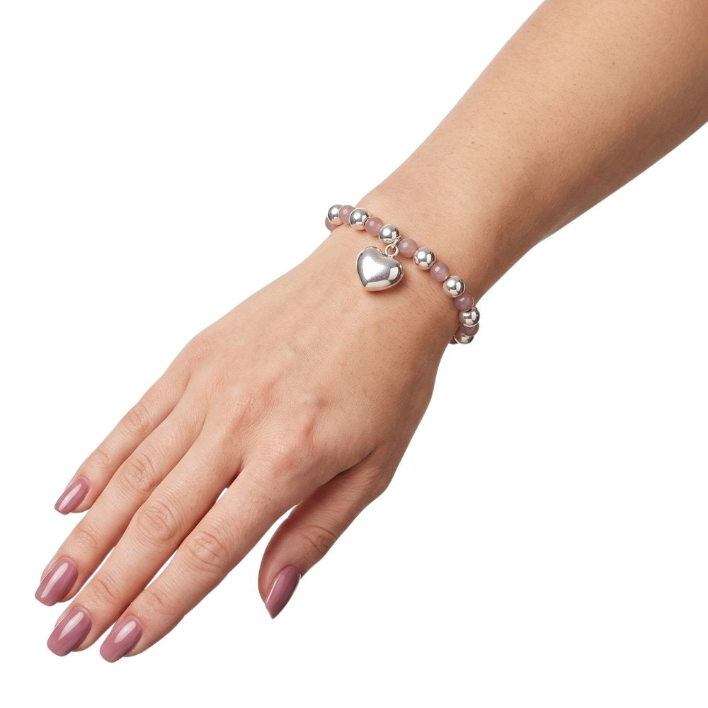 A silver charm bracelet with a heart-shaped pendant, cats eye and silver beads, shown worn on a woman's wrist against a plain white background.