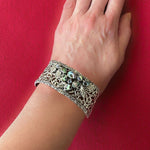 Decorative silver bracelet with abalone on a wrist against a red background