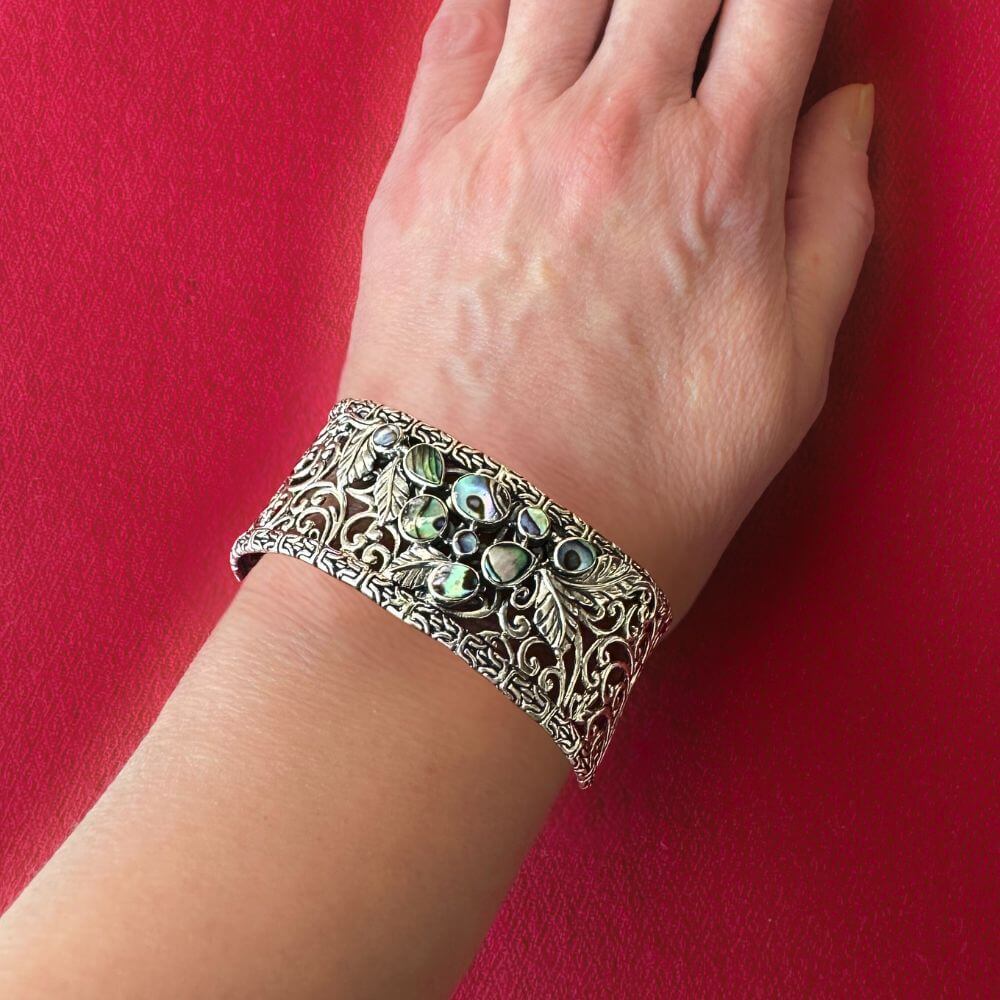 Decorative silver bracelet with abalone on a wrist against a red background