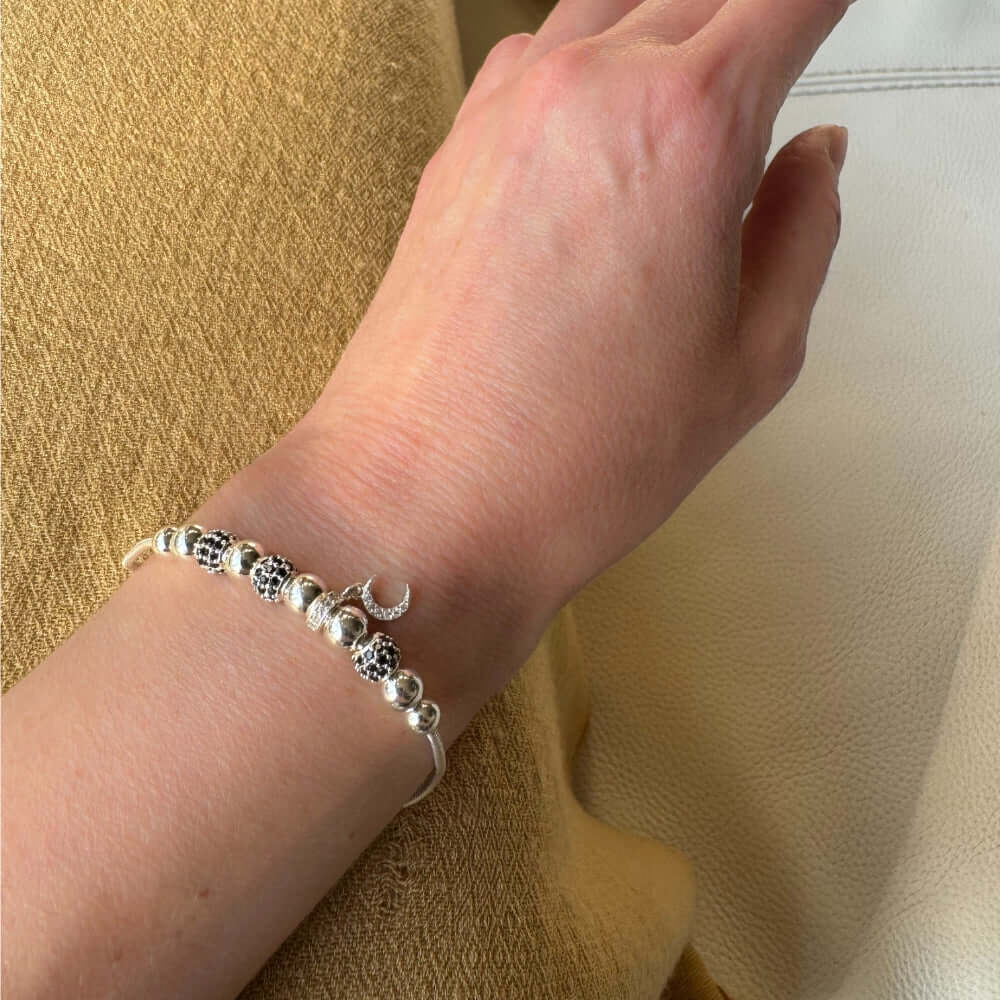 Silver bracelet with beads on a wrist against a beige background