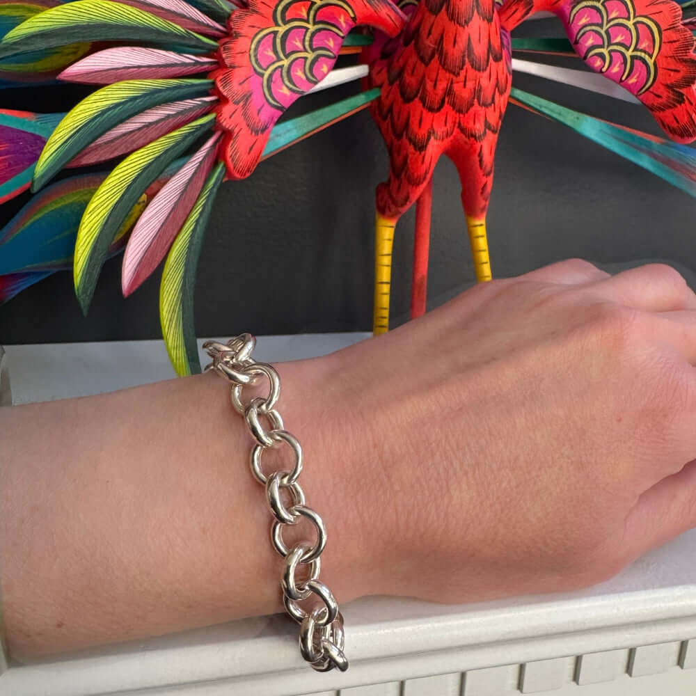 Silver chain bracelet on a wrist with a colorful parrot sculpture in the background