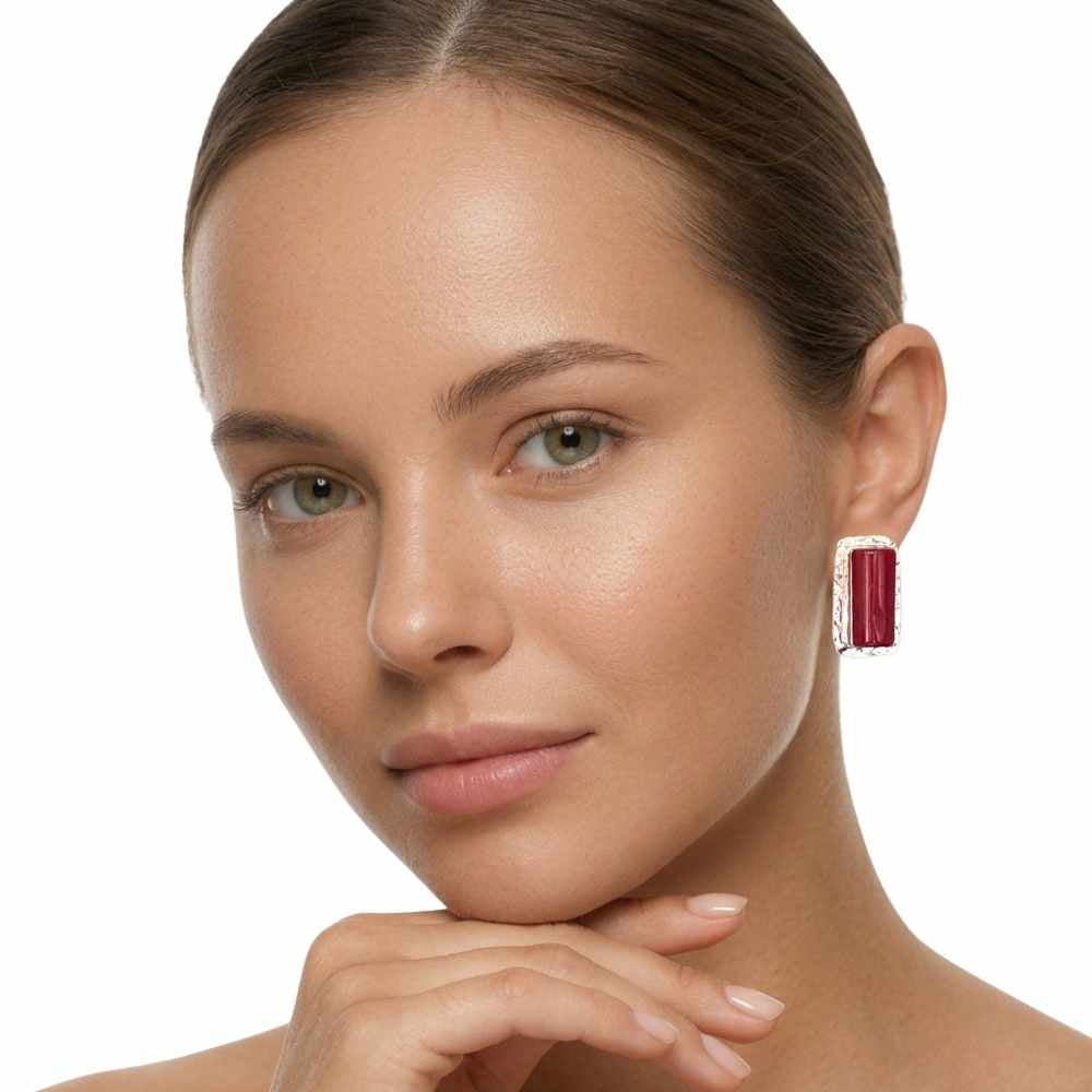 A close-up of a woman wearing a single rectangular drop earring with red coral and silver-toned borders, set against a plain white background.
