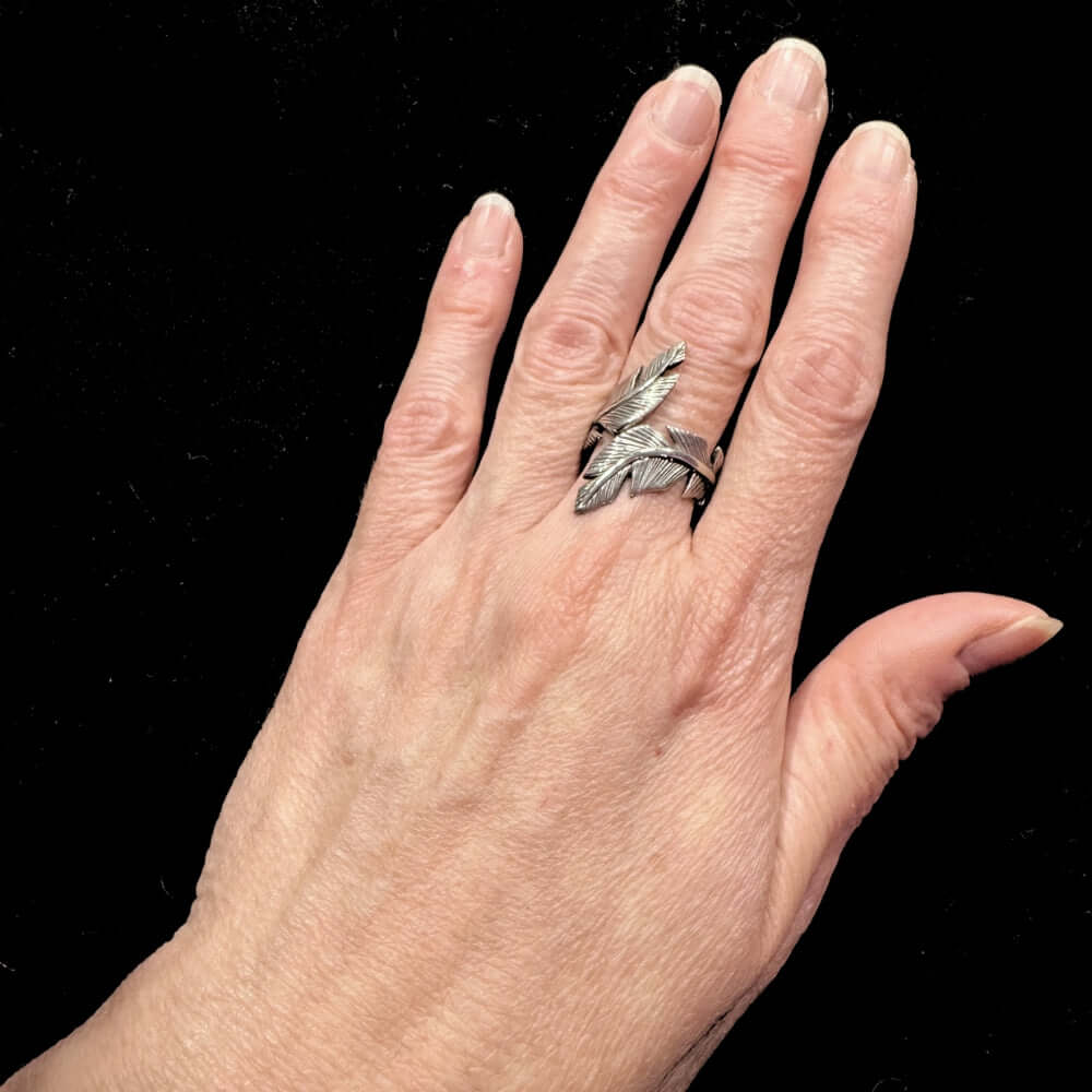 Hand wearing a silver feather ring against a black background