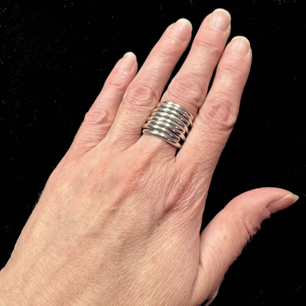Hand wearing a stack of silver rings on a black background